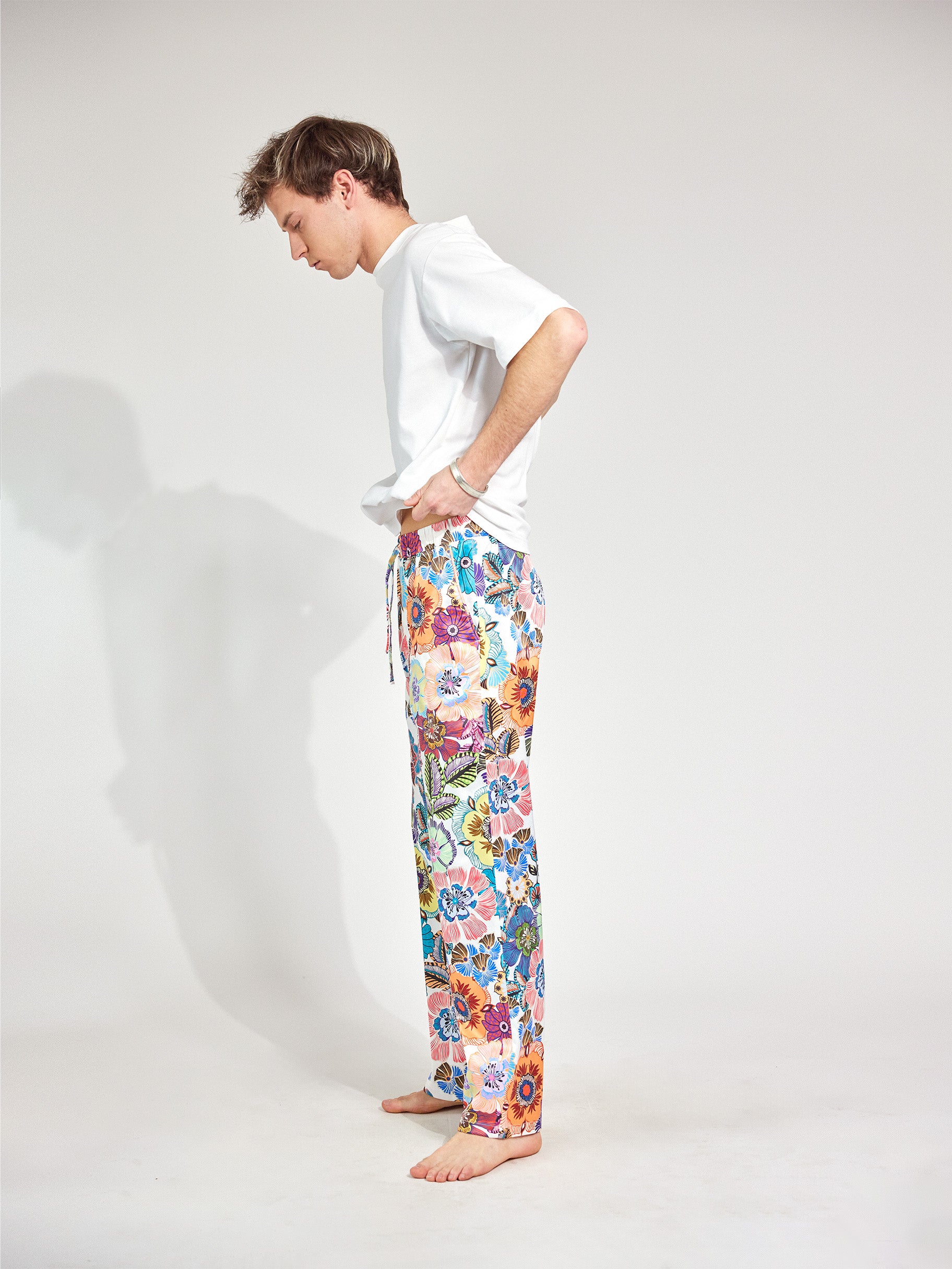 Mann trägt Hose im Pyjama-Style aus fließendem, glänzenden französischen Satinstoff und Bootcut-Schnitt und Blumenmuster