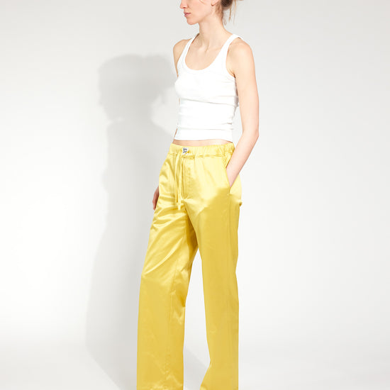 Frau trägt Hose im Pyjama-Style aus glänzendem Satin-Mix in Gold-Gelb mit tiefen Hosentaschen und Bootcut-Schnitt