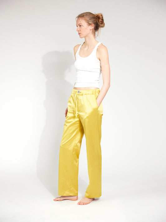 Frau trägt Hose im Pyjama-Style aus glänzendem Satin-Mix in Gold-Gelb mit tiefen Hosentaschen und Bootcut-Schnitt